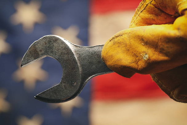 Worn work glove holding wrench tool above US American flag. Made in USA, American workforce, blue collar worker, or Labor Day concept. - Photo, Image
