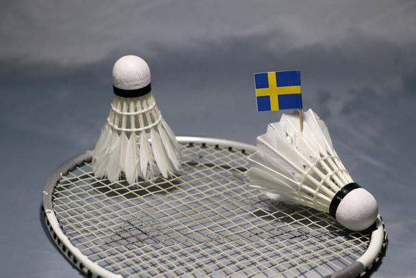 Mini kij flagowy Szwecji na wahadłowcu i kolejny wahadłowiec założony na siatkę rakiety badmintona na szarej podłodze.  - Zdjęcie, obraz