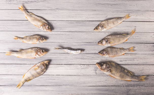Composition of dried fish on a wooden table. The big fish attacks the small fish. Studio photo. - Foto, Imagem