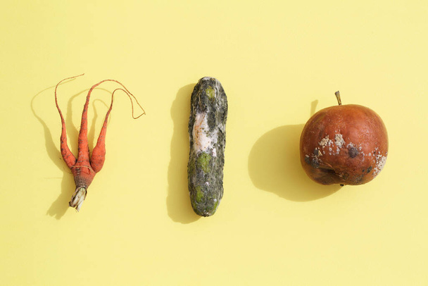  rotten apple, cucumber, carrot on yellow background. global hunger problem. overconsumption concept. - Photo, Image