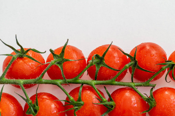une vigne de tomates cerises fraîches savoureuses horizontalement sur une table blanche - Photo, image
