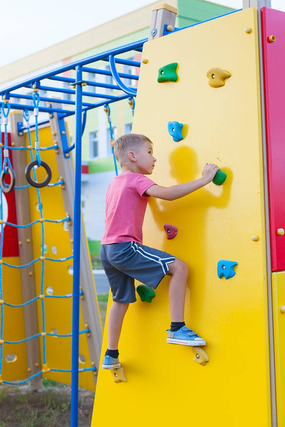 mały chłopiec wspinający się na skałę na placu zabaw w letni dzień - Zdjęcie, obraz
