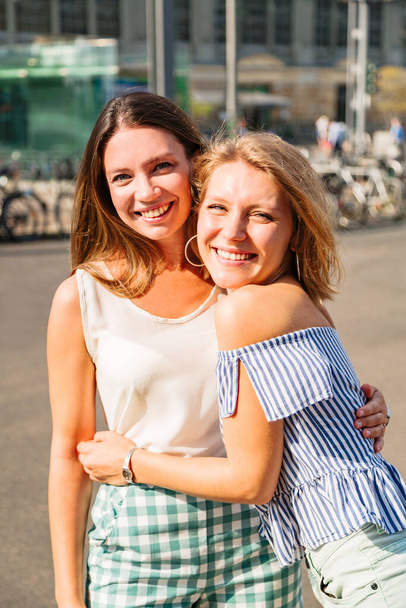 Blonde woman hugs her friend and smiles at camera - Foto, imagen