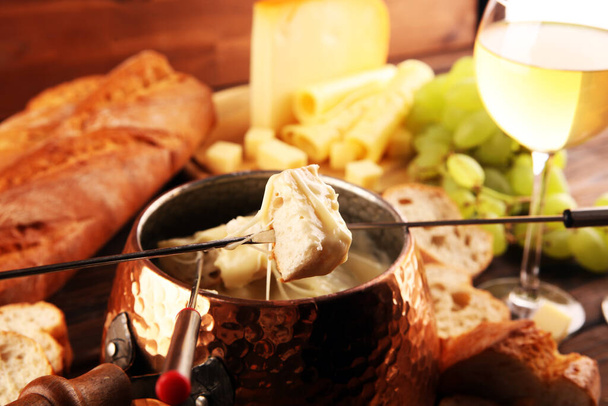 Dîner gourmand à la fondue suisse un soir d'hiver avec assortiment de fromages sur une planche à côté d'une casserole chauffée de fondue au fromage avec fourchettes trempant le pain  - Photo, image
