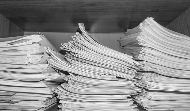 Papieren documenten opgestapeld in het archief. Documenten op de planken van de archiefkamer. Kantoorplanken in de kast vol met bestanden. zwart-wit foto - Foto, afbeelding
