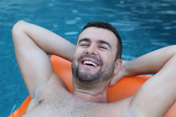 close-up portrait of handsome young man floating on inflatable mattress in swimming pool - Photo, Image