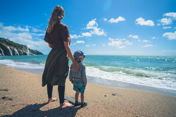 A young mother and her preschooler boy are standing on the beach on a sunny summer day - 写真・画像