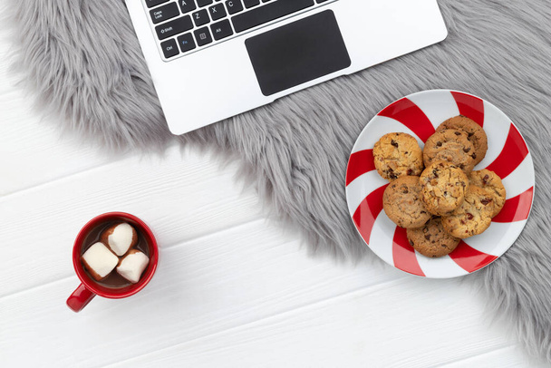 Laptop mit Kakao und Keksen auf pelzigem Hintergrund. Online-Weihnachtseinkauf funktioniert von zu Hause aus. - Foto, Bild