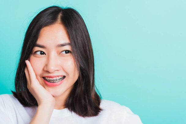 Portret azjatyckiej nastolatki piękny uśmiech młodej kobiety mają aparat dentystyczny na zębach śmiech dotyka jej twarz ręcznie, studio strzał izolowany na niebieskim tle, Medycyna i stomatologia koncepcja - Zdjęcie, obraz