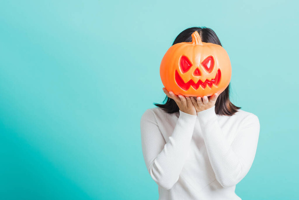 Portrait of Asian beautiful young woman holding orange model pumpkins at her head, funny happy female with ghost pumpkins, studio shot isolated on blue background - 写真・画像