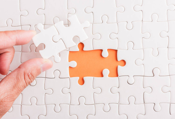 Top view flat lay of hand-holding last piece white paper jigsaw puzzle game last pieces put to place for solve problem complete mission, studio shot on an orange background, quiz calculation concept - Foto, immagini