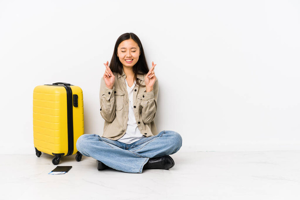 Молодая китайская путешественница, сидящая с посадочными талонами, скрещивает пальцы за удачу - Фото, изображение