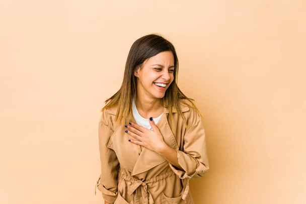 Young woman isolated on beige background laughing keeping hands on heart, concept of happiness. - Foto, imagen