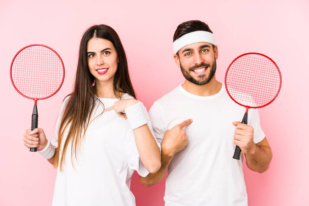 Young couple playing badminton isolated person pointing by hand to a shirt copy space, proud and confident - Foto, Imagen