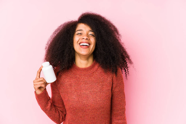 Jeune femme afro tenant une vitamine isolée Jeune femme afro tenant une hamster riant et s'amusant. - Photo, image