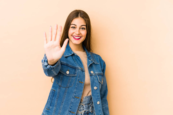 Young caucasian woman isolated en beige background smiling cheerful showing number five with fingers. - Photo, Image