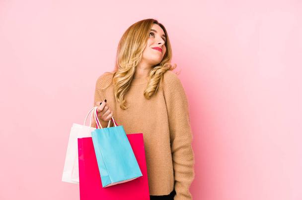 Young blonde woman holding shopping bags isolated dreaming of achieving goals and purposes - Foto, afbeelding