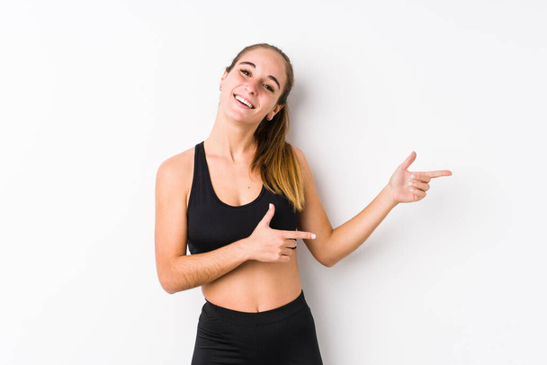 Young caucasian fitness woman posing in a white background excited pointing with forefingers away. - Foto, immagini
