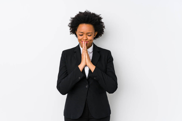 口の近くで祈るに手を保持隔離された白い背景を持つ中高年アフリカ系アメリカ人のビジネス女性は、自信を感じています. - 写真・画像