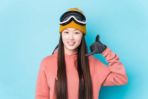 Jeune Chinoise vêtue de vêtements de ski isolés montrant un geste d'appel téléphonique mobile avec les doigts. - Photo, image