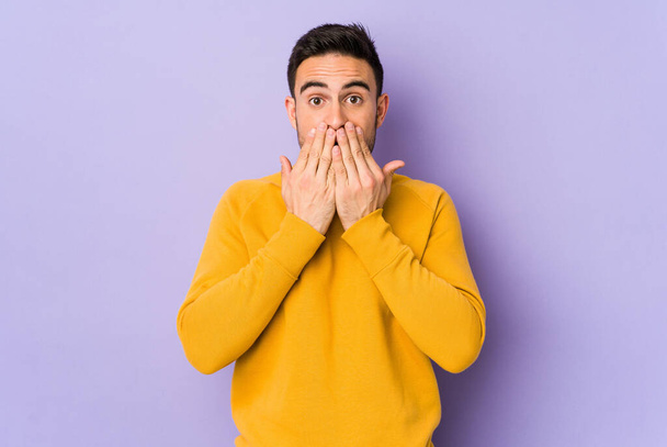 Young caucasian man isolated on purple background shocked, covering mouth with hands, anxious to discover something new. - Photo, image