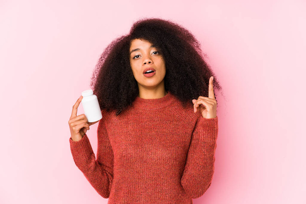 Young afro woman holding a vitamins isolated Young afro woman holding a vitaminshaving some great idea, concept of creativity. - Фото, зображення