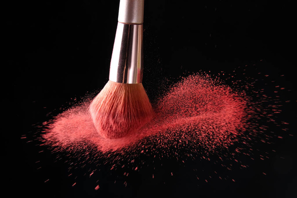Makeup brush and burst of cosmetics on dark background - Photo, Image