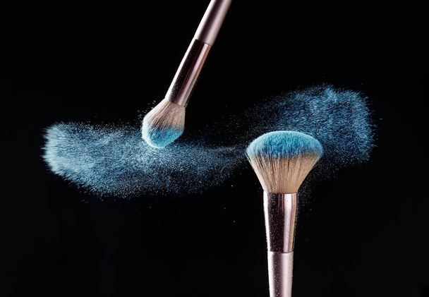 Makeup brushes and burst of cosmetics on dark background - Foto, imagen