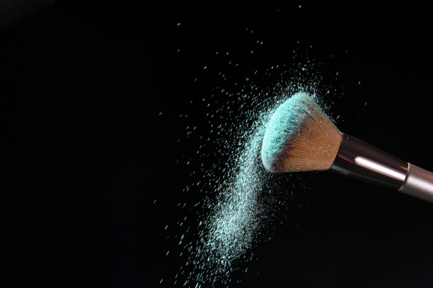 Cepillo de maquillaje y explosión de cosméticos sobre fondo oscuro - Foto, Imagen