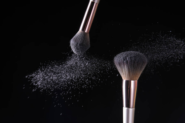 Makeup brushes and burst of cosmetics on dark background - Foto, Imagen
