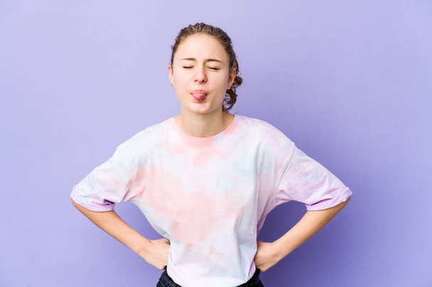 Young caucasian woman on purple background funny and friendly sticking out tongue. - Photo, Image