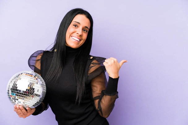Женщина, держащая мяч партии изолированы на фиолетовых фоновых точках с большим пальцем прочь, смеясь и беззаботно. - Фото, изображение
