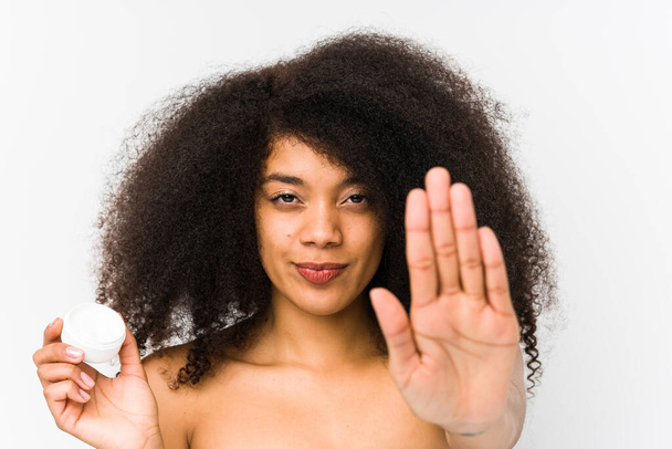 Young afro woman holding a moisturizer isolated standing with outstretched hand showing stop sign, preventing you. - Foto, afbeelding