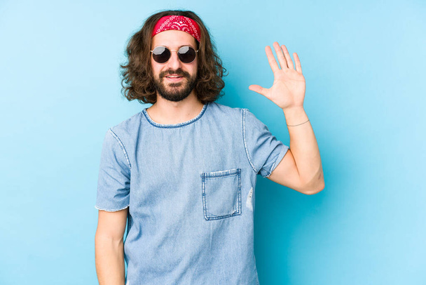Jeune homme aux cheveux longs portant un festival hipster regarder isolé souriant gai montrant numéro cinq avec les doigts. - Photo, image
