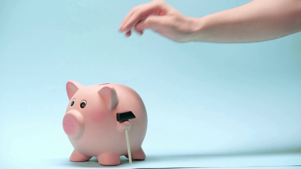 Καλλιεργημένη άποψη του ανθρώπου βάζοντας χρήματα σε κουμπαρά σε μπλε φόντο - Πλάνα, βίντεο