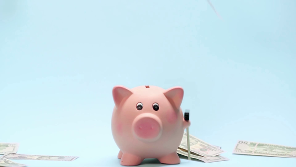 Zeitlupe des Geldes fällt neben Sparschwein auf blauem Hintergrund - Filmmaterial, Video