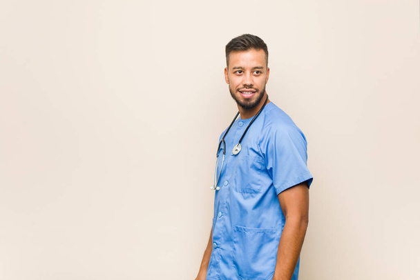 Jeune infirmière sud-asiatique homme regarde de côté souriant, gai et agréable. - Photo, image