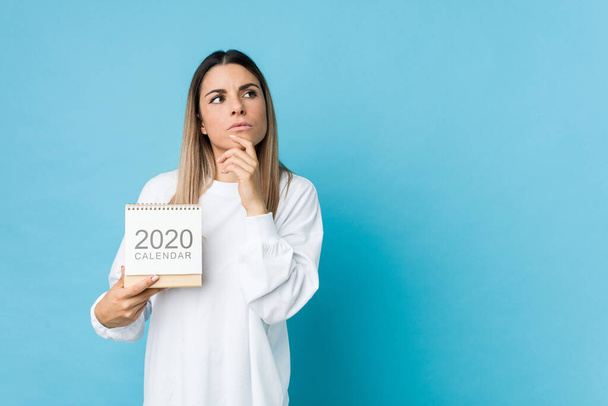 Mulher caucasiana jovem segurando um calendário 2020 olhando para os lados com expressão duvidosa e cética. - Foto, Imagem