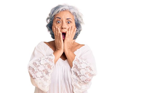Seniorin mit grauen Haaren trägt Boheme-Stil Angst und Schock, Überraschung und erstaunten Gesichtsausdruck mit den Händen auf dem Gesicht  - Foto, Bild