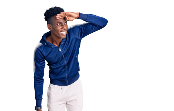 スポーツウェアを身に着けている若いアフリカ系アメリカ人の男性は、頭の上に手で遠くを見て非常に幸せと笑顔。検索の概念.  - 写真・画像