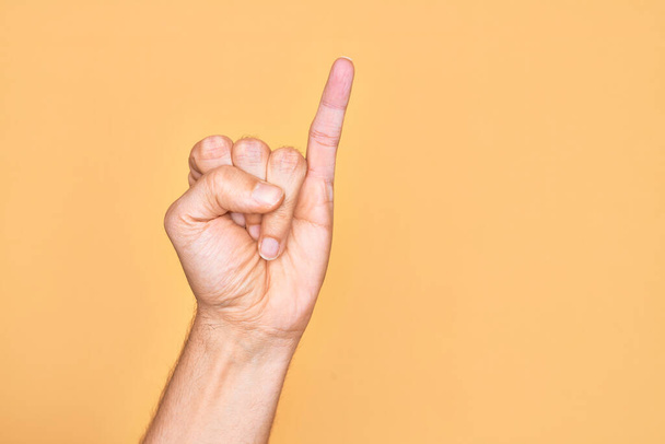Kafkasyalı bir gencin parmağı, izole edilmiş sarı arka planda serçe parmağı, bir numaralı söz sözü olarak gösteriyor. - Fotoğraf, Görsel