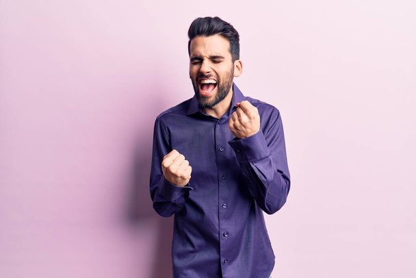 Young handsome man with beard wearing casual shirt celebrating surprised and amazed for success with arms raised and eyes closed. winner concept.  - Fotoğraf, Görsel