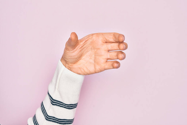 Valkoihoisen nuorukaisen käsi näyttää sormiaan vaaleanpunaisella taustalla pitäen näkymätöntä esinettä, tyhjä käsi leikaten ja tarttuen eleeseen. - Valokuva, kuva