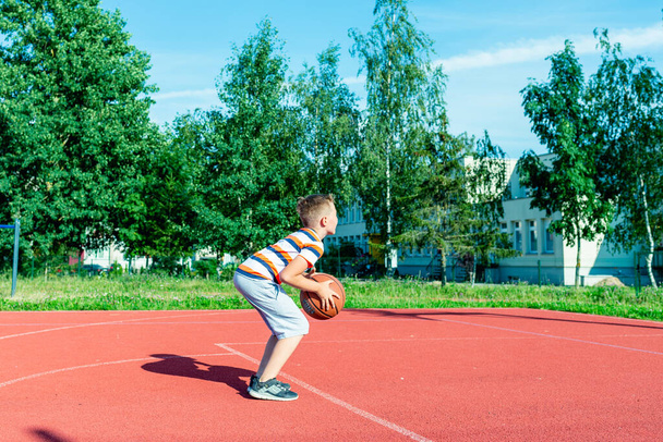 Telsiai,Lithuania 08 12 2020 Attractive caucasian little basketball player training on a outdoors red court - Фото, изображение