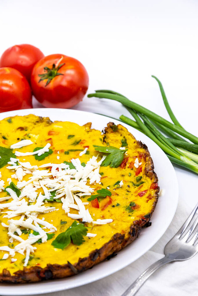 leckeres Omelett serviert mit frischen grünen Zwiebeln und Tomaten und geriebenem Käse auf weißem Dekor - Foto, Bild