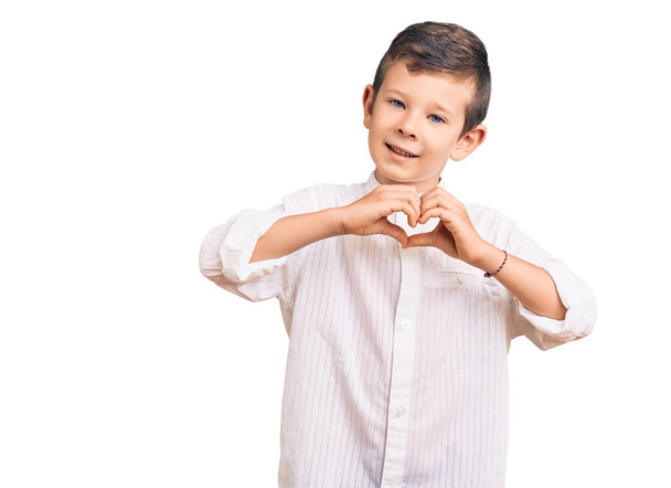 Lindo niño rubio con camisa elegante sonriendo en el amor haciendo forma de símbolo del corazón con las manos. concepto romántico.  - Foto, Imagen