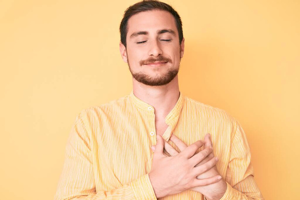 Young handsome man wearing casual clothes smiling with hands on chest with closed eyes and grateful gesture on face. health concept.  - Photo, Image