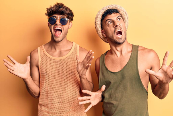 Giovane coppia gay indossa vestiti estivi pazzo e pazzo urlando e urlando con espressione aggressiva e braccia alzate. concetto di frustrazione.  - Foto, immagini