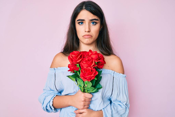 Brunette teenager girl holding flowers depressed and worry for distress, crying angry and afraid. sad expression.  - Foto, imagen