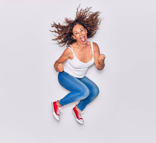 Middle age beautiful hispanic woman wearing casual clothes smiling happy. Jumping with smile on face doing winner gesture with fists up over isolated white background - Fotografie, Obrázek